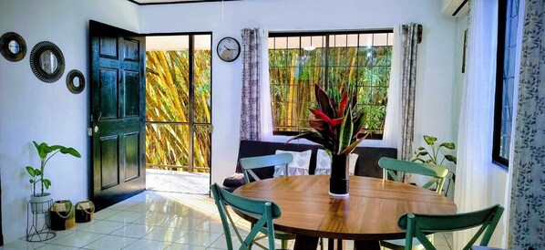 A dining area with a round wooden table, four chairs, a potted plant, and a window with bamboo outside. - Fully Equipped Kitchen Privacy & Pura Vida (Quepos)
