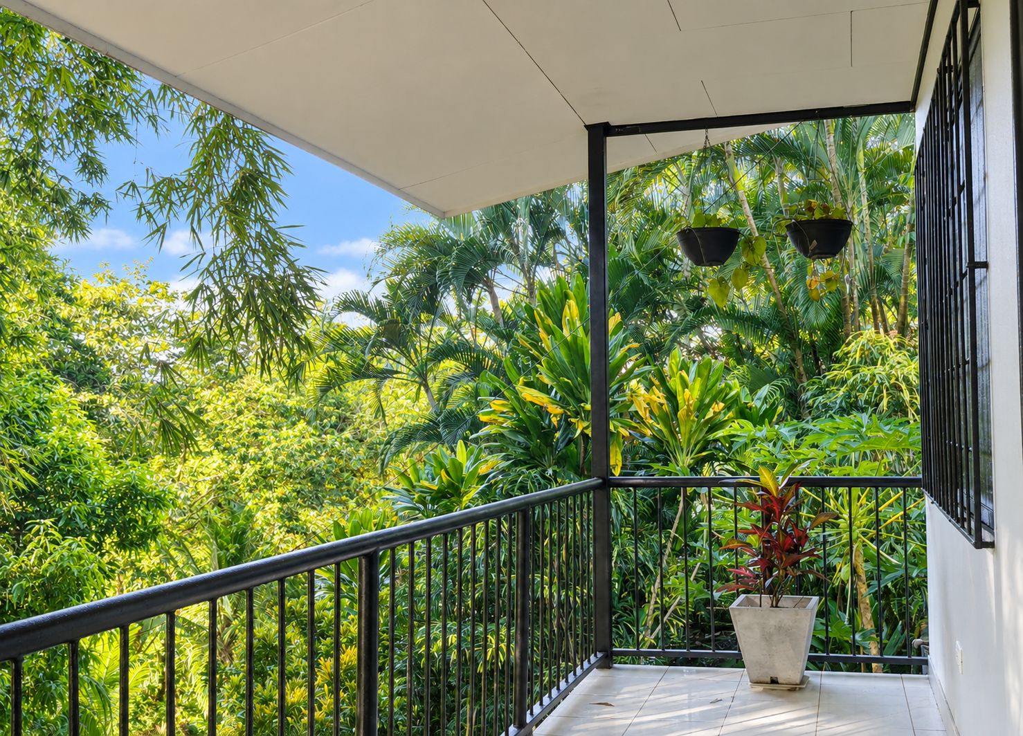 Un balcon donnant sur une végétation tropicale luxuriante, avec une plante en pot et un luminaire suspendu.