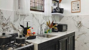 A kitchen with marble walls, a gas stove, a sink, and a window with curtains. - Fully Equipped Kitchen Privacy & Pura Vida (Quepos)