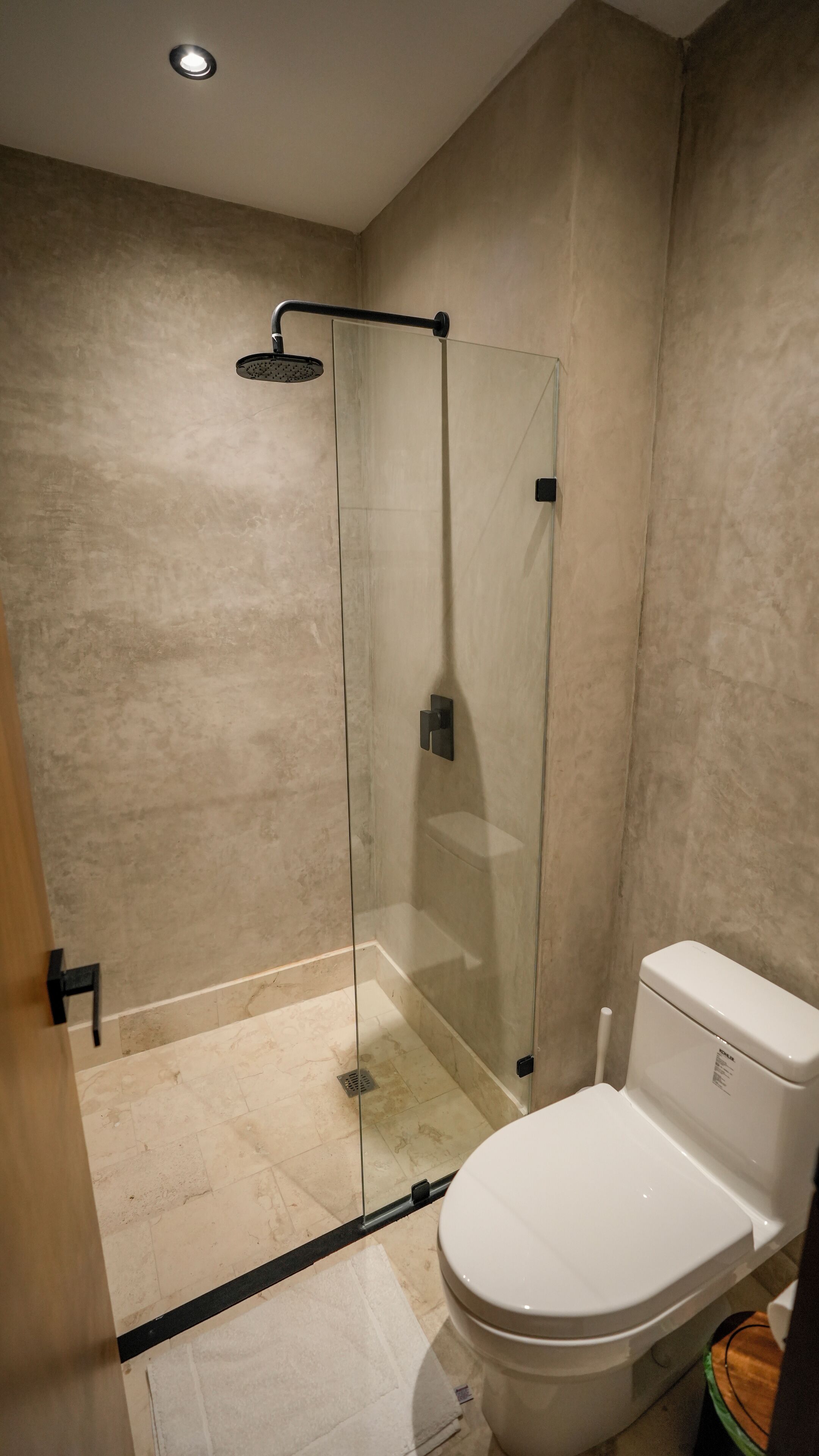 A modern bathroom with a glass-enclosed shower, a toilet, and a tiled floor.