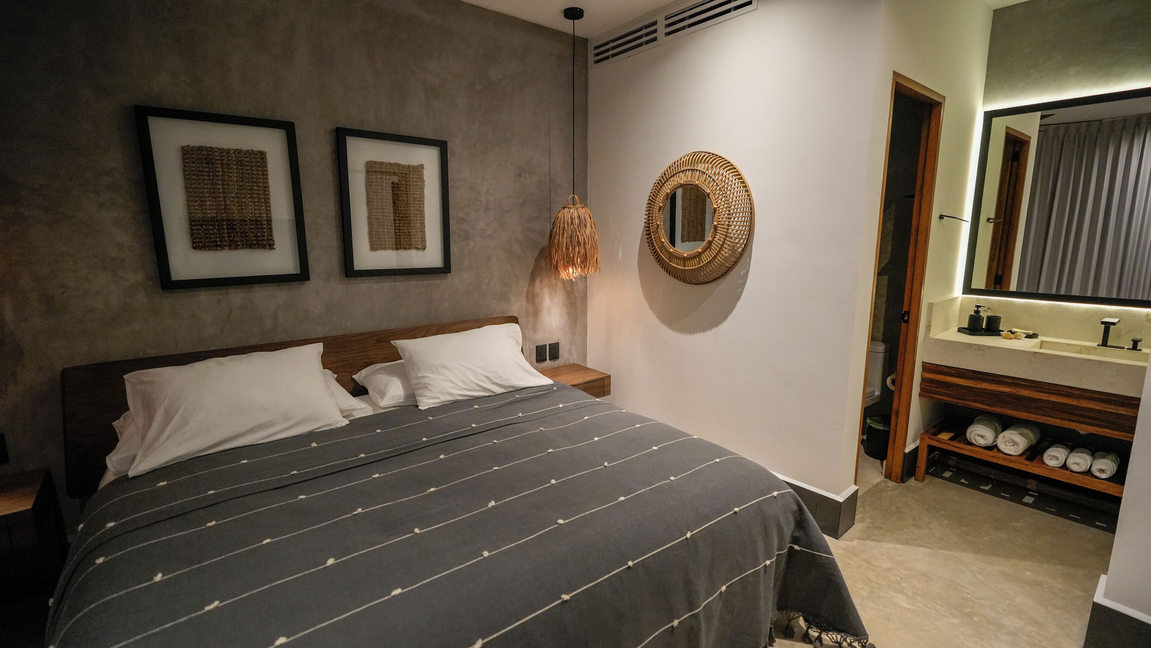 Un dormitorio ordenado con una cama, mesitas de noche, un espejo en la pared y un estante empotrado con toallas.