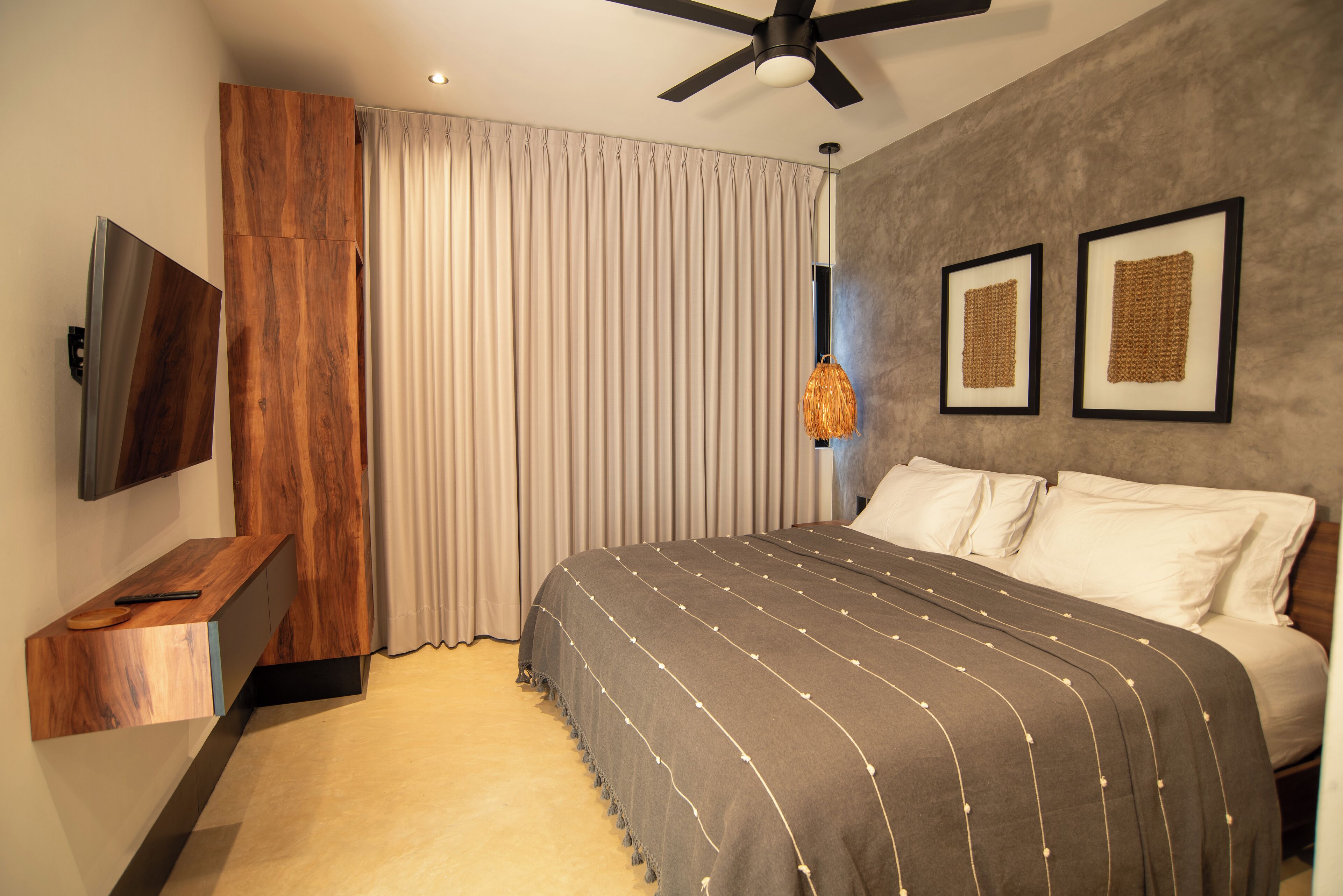 Une chambre moderne avec un grand lit, un ventilateur de plafond, un téléviseur fixé au mur et une commode en bois.