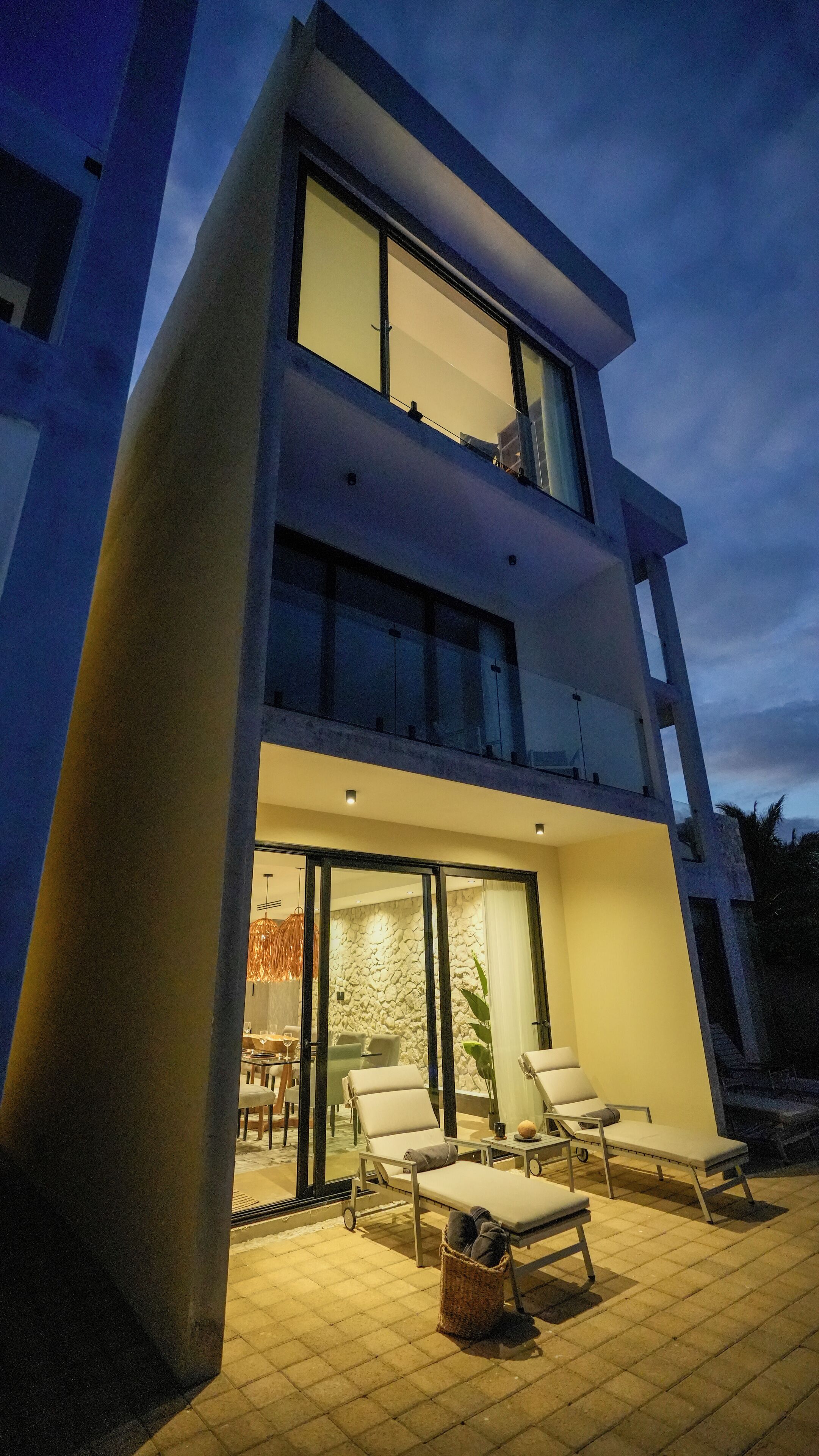 A modern two-story building with a balcony, outdoor seating area, and a stone wall interior.