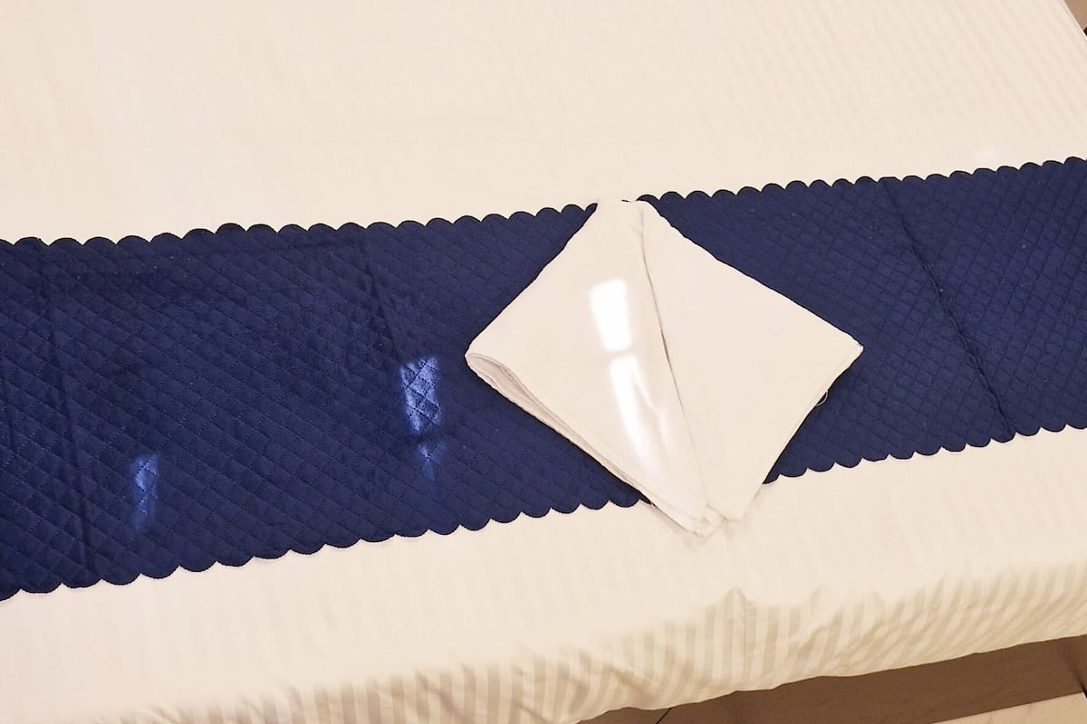 A bed with white bedding and a blue quilted blanket.