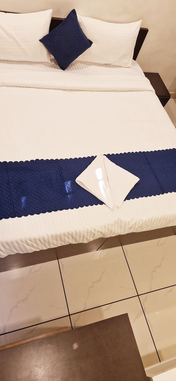 Ein Bett mit weißer Bettwäsche und einer blauen gesteppten Decke.