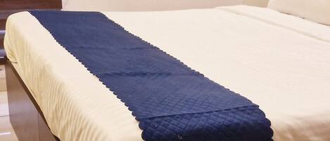 Un letto con materasso bianco e coperta blu, una testiera in legno e un pavimento piastrellato.