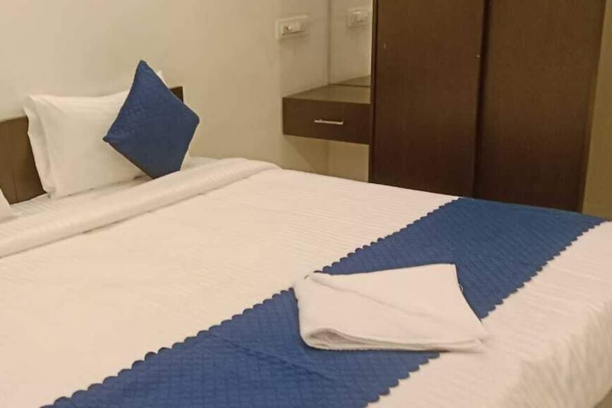A neatly made bed with a white and blue bedspread, two pillows, and a folded white towel on the side.