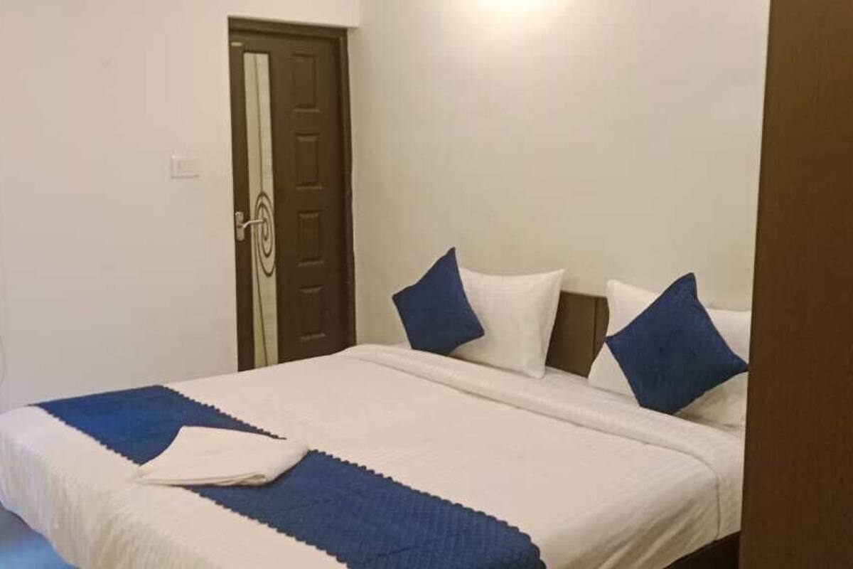 A neatly made bed with a blue and white bedspread and pillows, a wooden door, and a white wall.