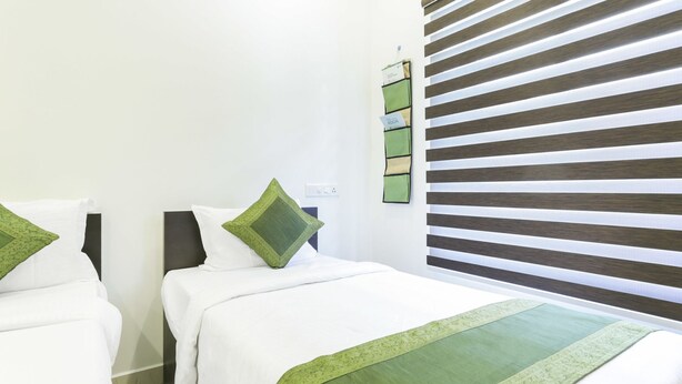 A hotel room with two beds, each with white bedding and green accents. There is a wall-mounted control panel with a green and beige color scheme. - Hotel F Sqaure  (Kochi)