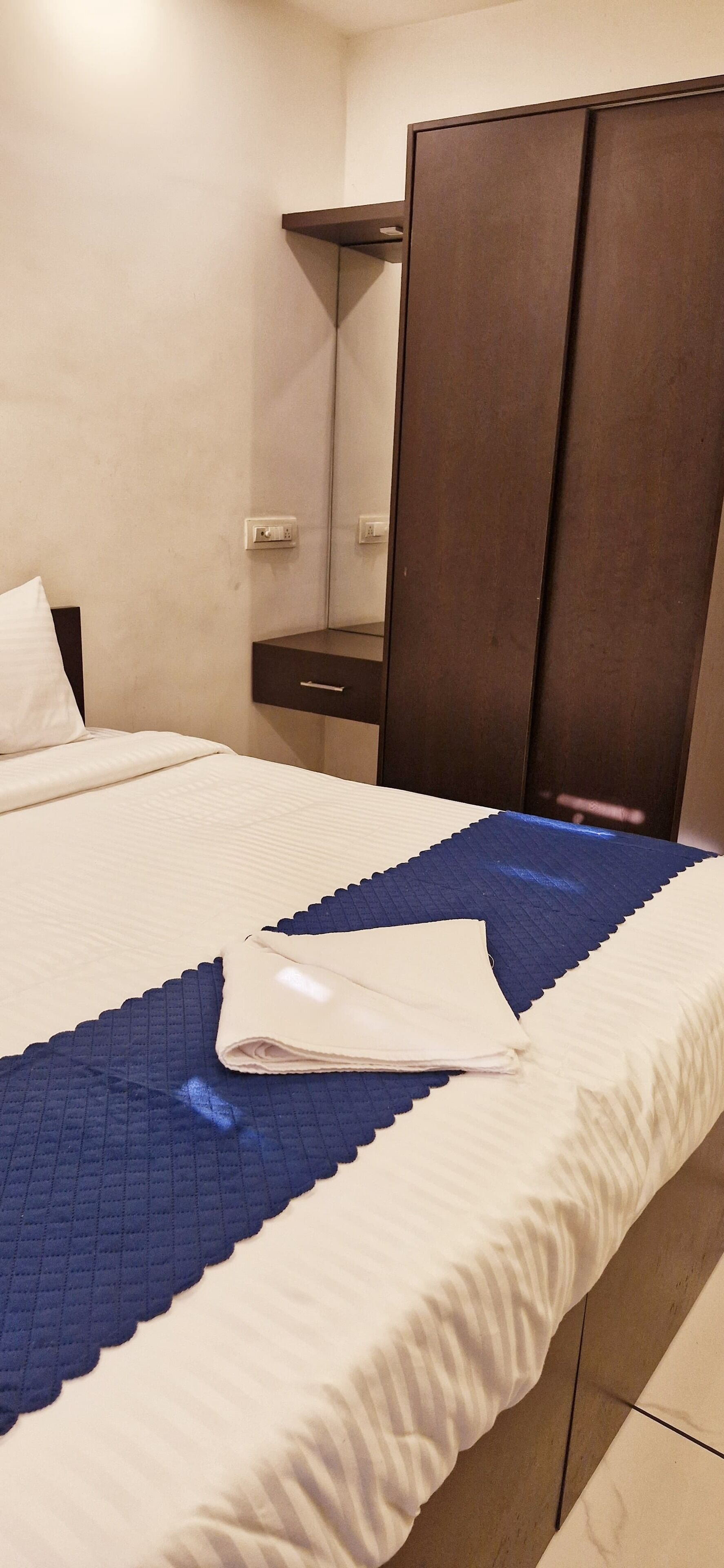 Una cama bien hecha con colcha azul y blanca, una almohada blanca y una toalla blanca doblada sobre la cama.