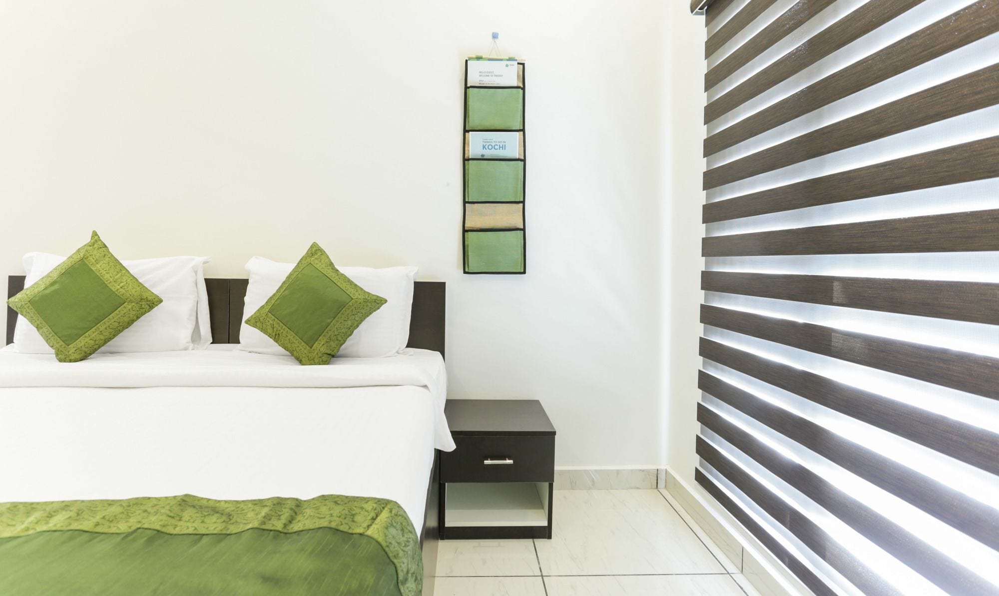 Un dormitorio con cama, dos almohadas, una mesita de noche y un termostato en la pared.
