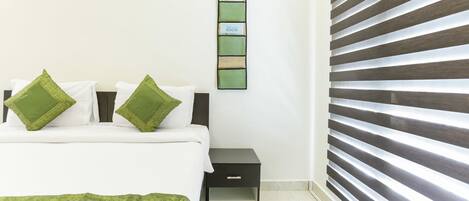 Un dormitorio con cama, dos almohadas, una mesita de noche y un termostato en la pared.