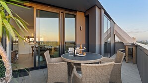 A modern balcony with wicker furniture, a glass door leading to an indoor area, and a scenic view. - Zi apartments - Balcony, Bayview, Sauna & Pool (South Melbourne)