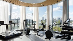 A modern gym with treadmills, elliptical machines, and a rowing machine, featuring large windows and a city view. - Zi apartments - Balcony, Bayview, Sauna & Pool (South Melbourne)