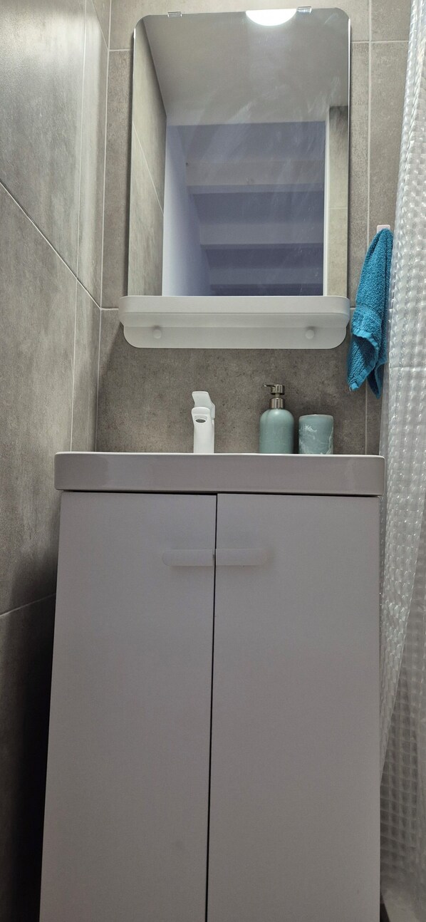 Une salle de bain avec un meuble-lavabo blanc, un miroir et deux bouteilles de savon posées sur le comptoir.