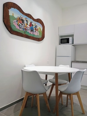 A dining area with a white table and chairs, a wooden-framed painting, and white kitchen cabinets.