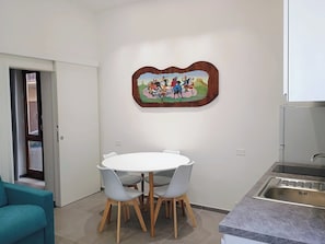 Un coin repas avec une table ronde et des chaises, une cuisine dotée d’un évier en acier inoxydable et une œuvre d’art accrochée au mur.