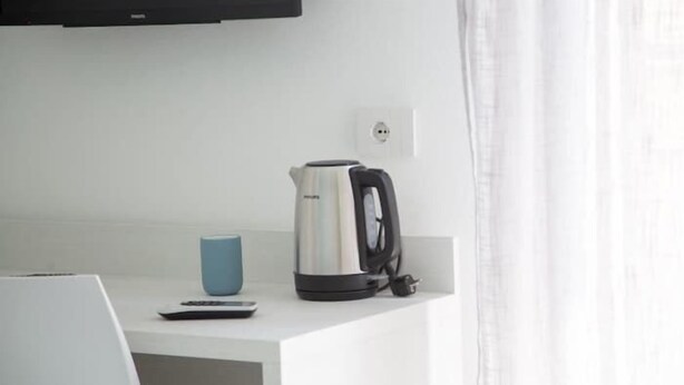 A white kitchen counter with a kettle, a blue mug, and a remote control.