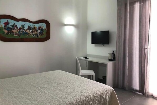 Habitación de hotel con cama, un escritorio con silla, televisor y un cuadro en la pared.