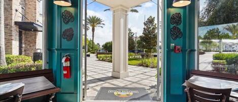 Entrada de hotel con una decoración color turquesa, un extintor y un felpudo con un diseño de sol y palmeras.