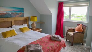 Een slaapkamer met een bed, een stoel, een schilderij en een raam met gordijnen.