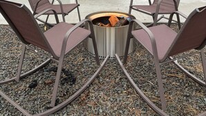 An outdoor patio with a fire pit, seating, and a building in the background.