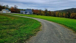 A gravel path leading to a house with a blue roof, surrounded by green fields and autumn-colored trees.