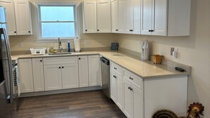A modern kitchen with white cabinets, a dishwasher, and a wooden floor.