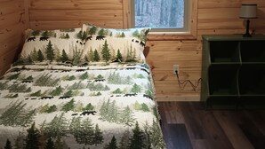 A wooden cabin bedroom with a bed, a window, a wall-mounted air conditioner, and a green nightstand.
