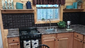 A cozy kitchen with wooden cabinets, a stove, and a window with curtains.