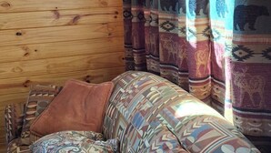 A cozy cabin interior with a wooden wall, a sign reading "Rk Old Friend," and a patterned sofa with a brown throw pillow.
