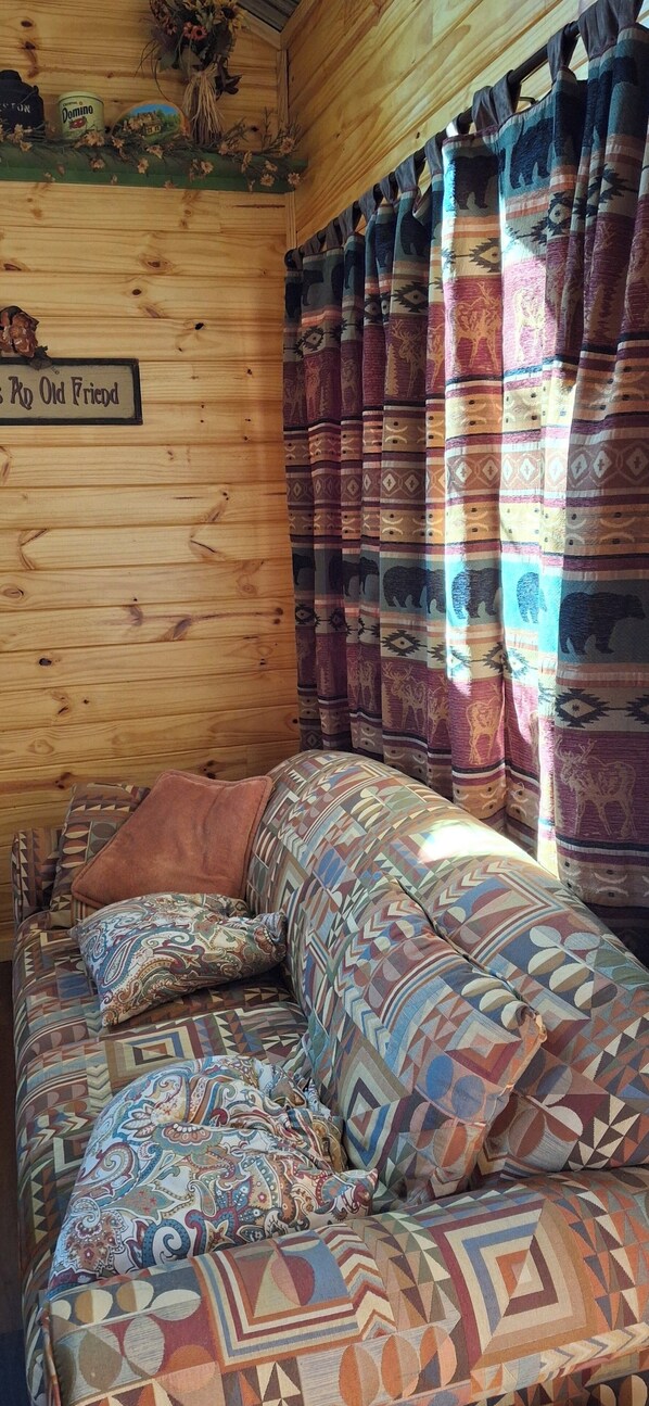 L’intérieur chaleureux d’un chalet avec un mur en bois, une enseigne indiquant « Rk Old Friend » et un canapé à motifs agrémenté d’un coussin marron.