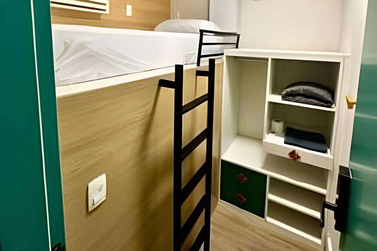 A compact room with a bunk bed, a ladder, a small desk, and a shelf with storage.