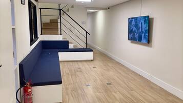 Una habitación amplia con piso de madera, un sofá azul, una escalera y un televisor montado.
