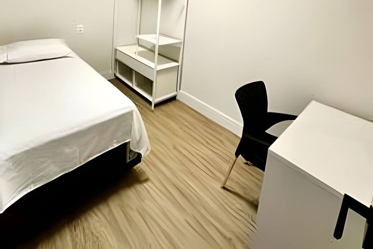 A room with a bed, a desk, a chair, and a white wardrobe.