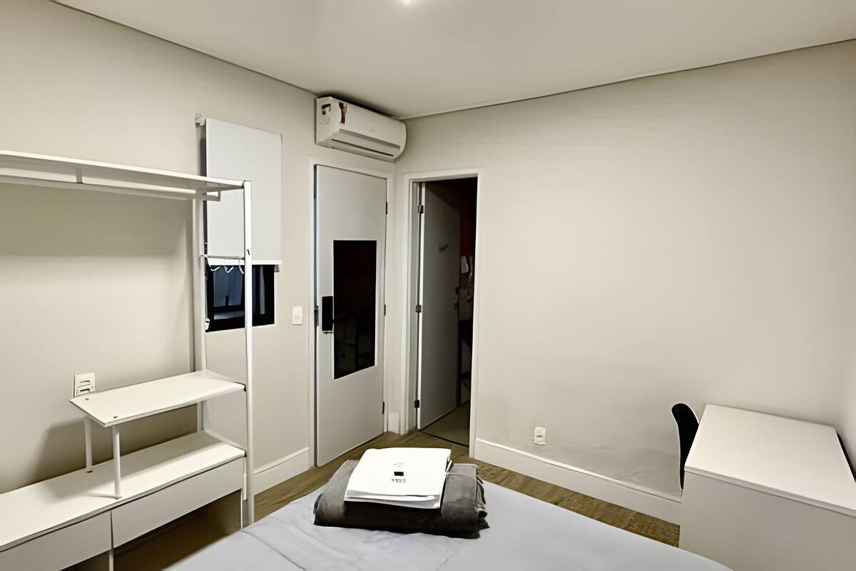 A bedroom with a bed, a desk, a wardrobe, and a door leading to another room.
