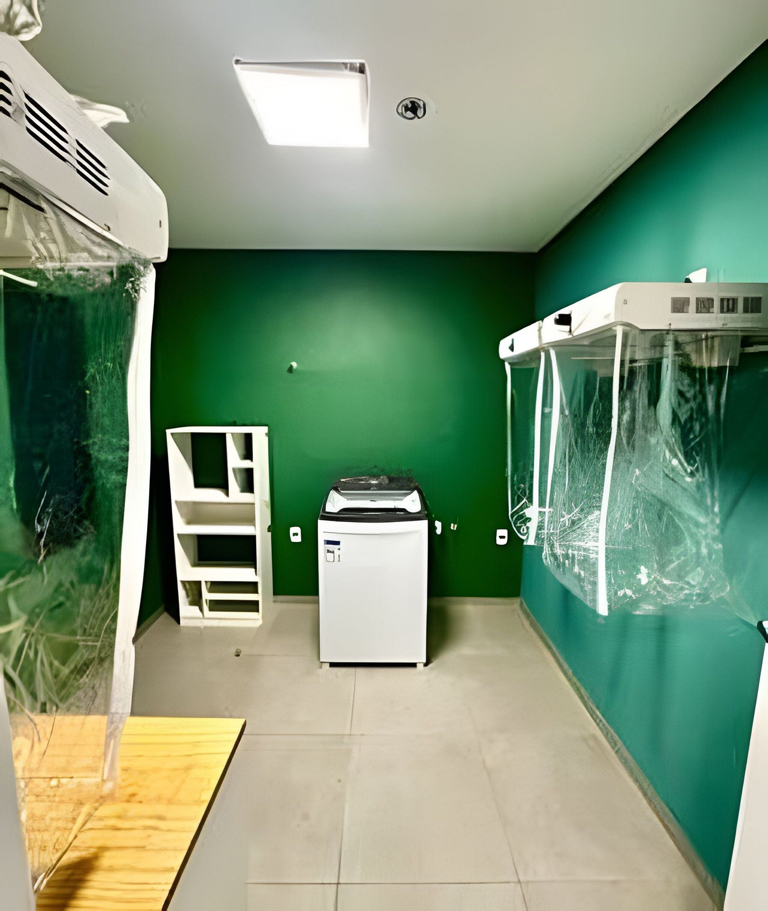 Una habitación con un aire acondicionado blanco, un calentador blanco, un refrigerador blanco y una pared verde.