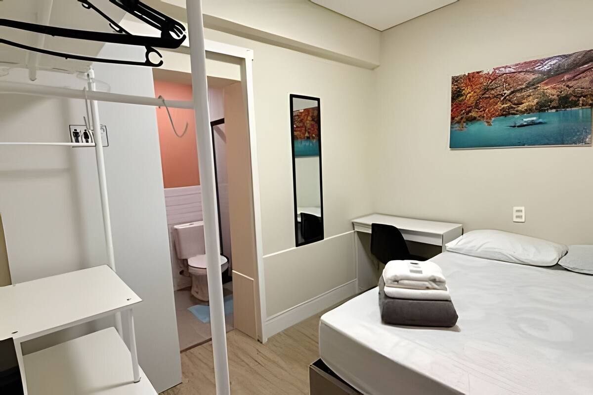 A bedroom with a bed, a desk, a mirror, a wardrobe, and a bathroom.