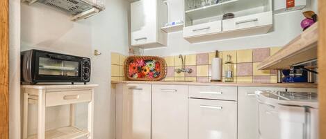 A compact kitchen with white cabinets, a microwave, a toaster oven, and a tiled backsplash.
