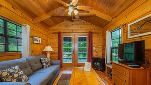 A cozy cabin interior with a wooden ceiling, a sofa, a coffee table, a TV, and a fireplace. - Blue Ridge Mountains Cabin | Engadine Inn & Cabins (Candler)