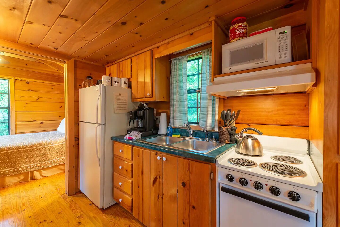 A compact kitchen with wooden cabinets, a refrigerator, a microwave, a stove, and a sink.