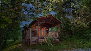A rustic cabin with a wooden deck, surrounded by dense foliage. - Smoky Mountains Cabin | Engadine Inn & Cabins (Candler)