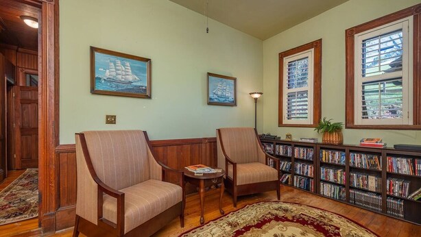 A library with two armchairs, a bookshelf, and a patterned rug. - Mary Hoyt Suite | Engadine Inn & Cabins (Candler)