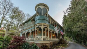 A two-story house with a wrap-around porch, a turret, and a flag. - Mary Hoyt Suite | Engadine Inn & Cabins (Candler)