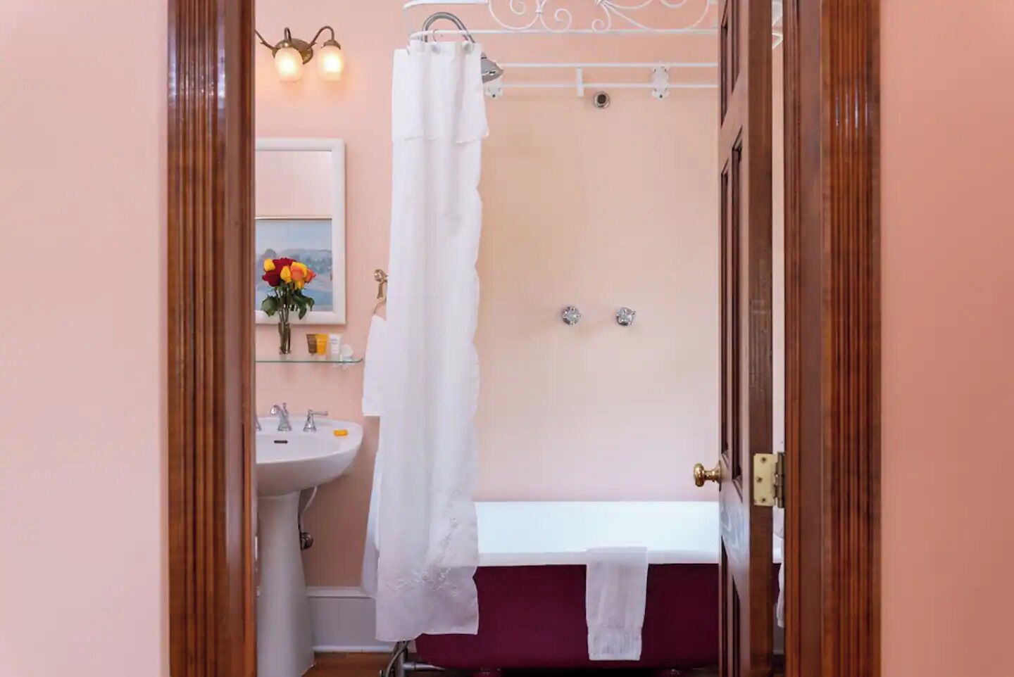 A bathroom with a white sink, a mirror, a shower curtain, and a red bathtub.