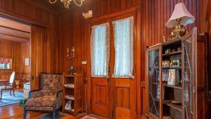 Une pièce aux murs lambrissés, avec un fauteuil à motifs, une bibliothèque et un tapis rouge.