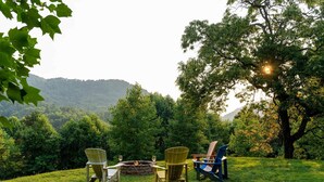 A grassy outdoor area with three Adirondack chairs and a fire pit. - Brickell Suite - Engadine Inn and Cabins (Candler)