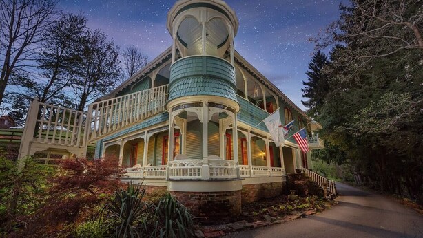 A large, two-story house with a wrap-around porch and a turret. - Brickell Suite - Engadine Inn and Cabins (Candler)