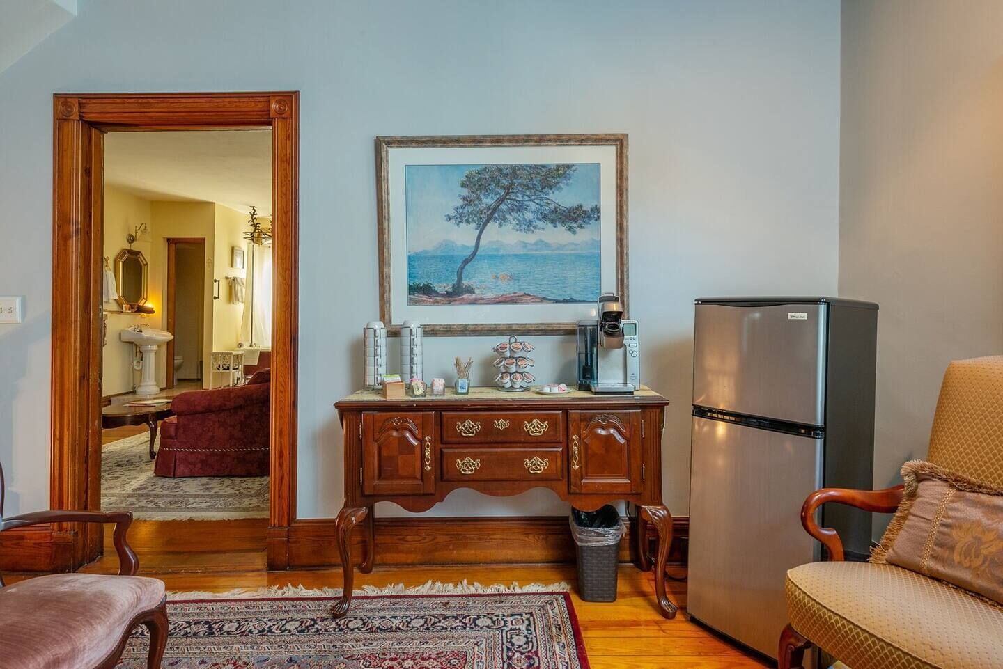 A living room with a wooden cabinet, a coffee machine, a refrigerator, a chair, and a rug.
