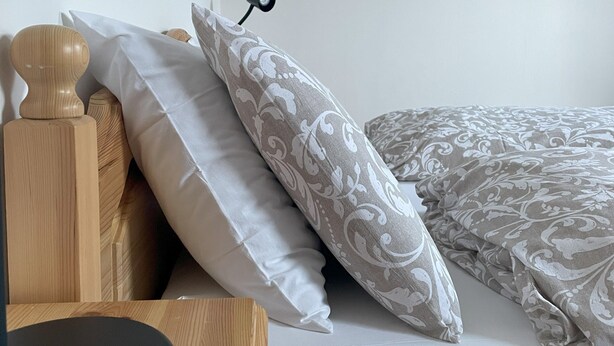 Cama bem arrumada com almofadas estampadas e mesa de cabeceira de madeira com abajur.
